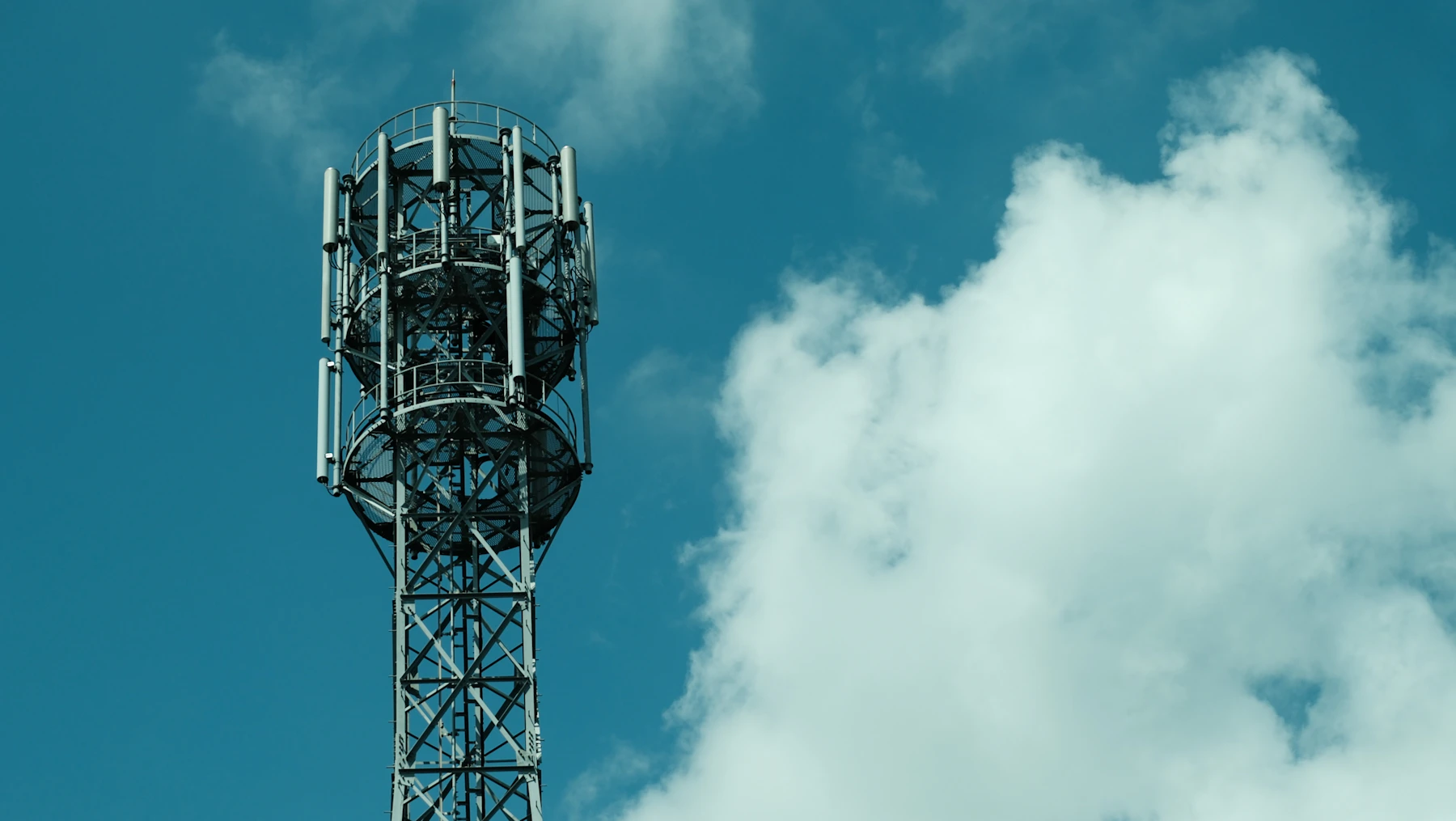 A mobile communications antenna tower against a blue sky with drifting clouds